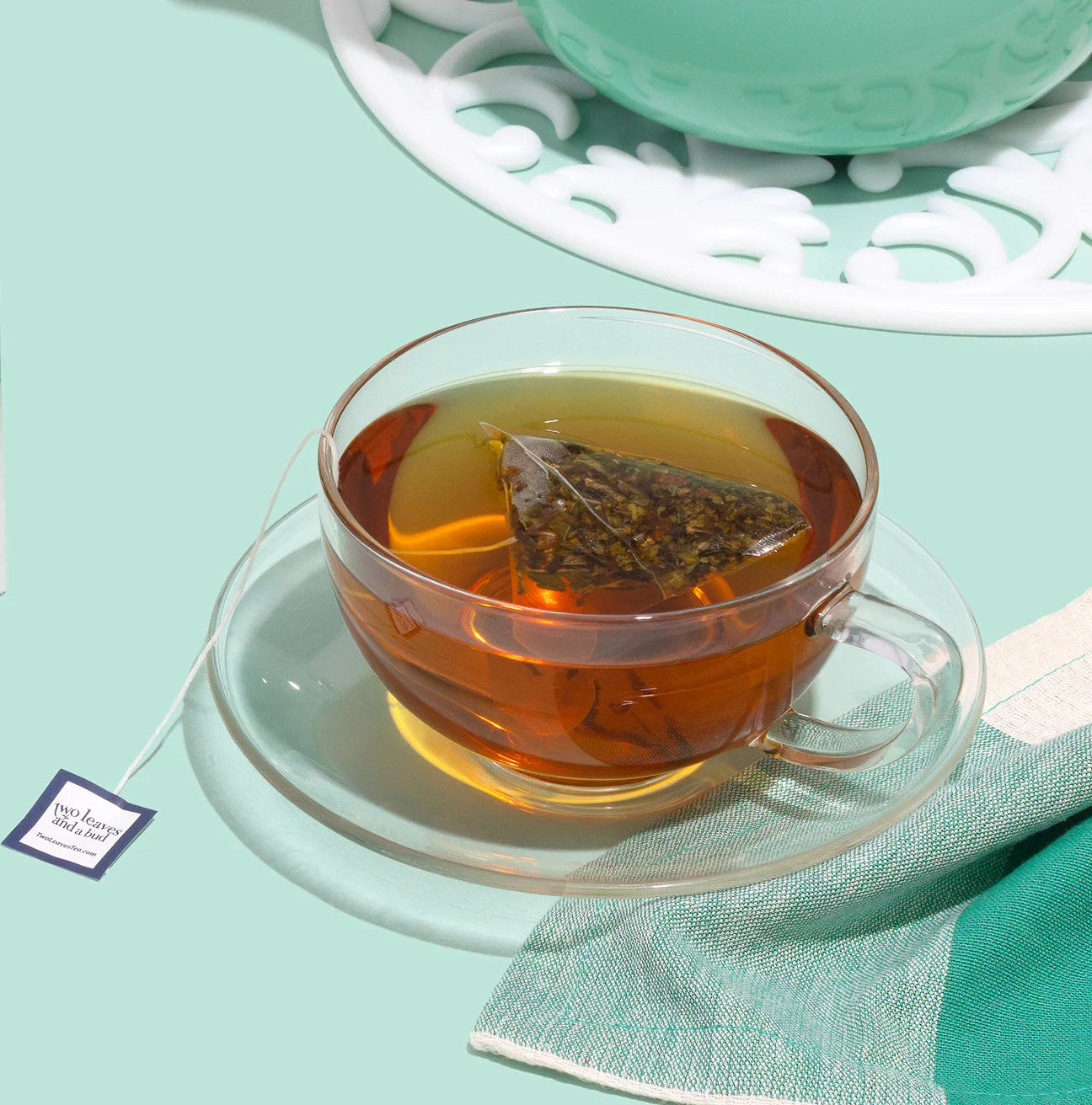 Clear glass cup with tea and a tea bag on a light green background