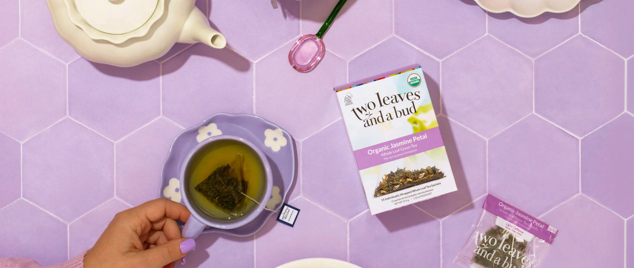 Tea cup with a hand, tea packaging, and teapot on a purple tiled background