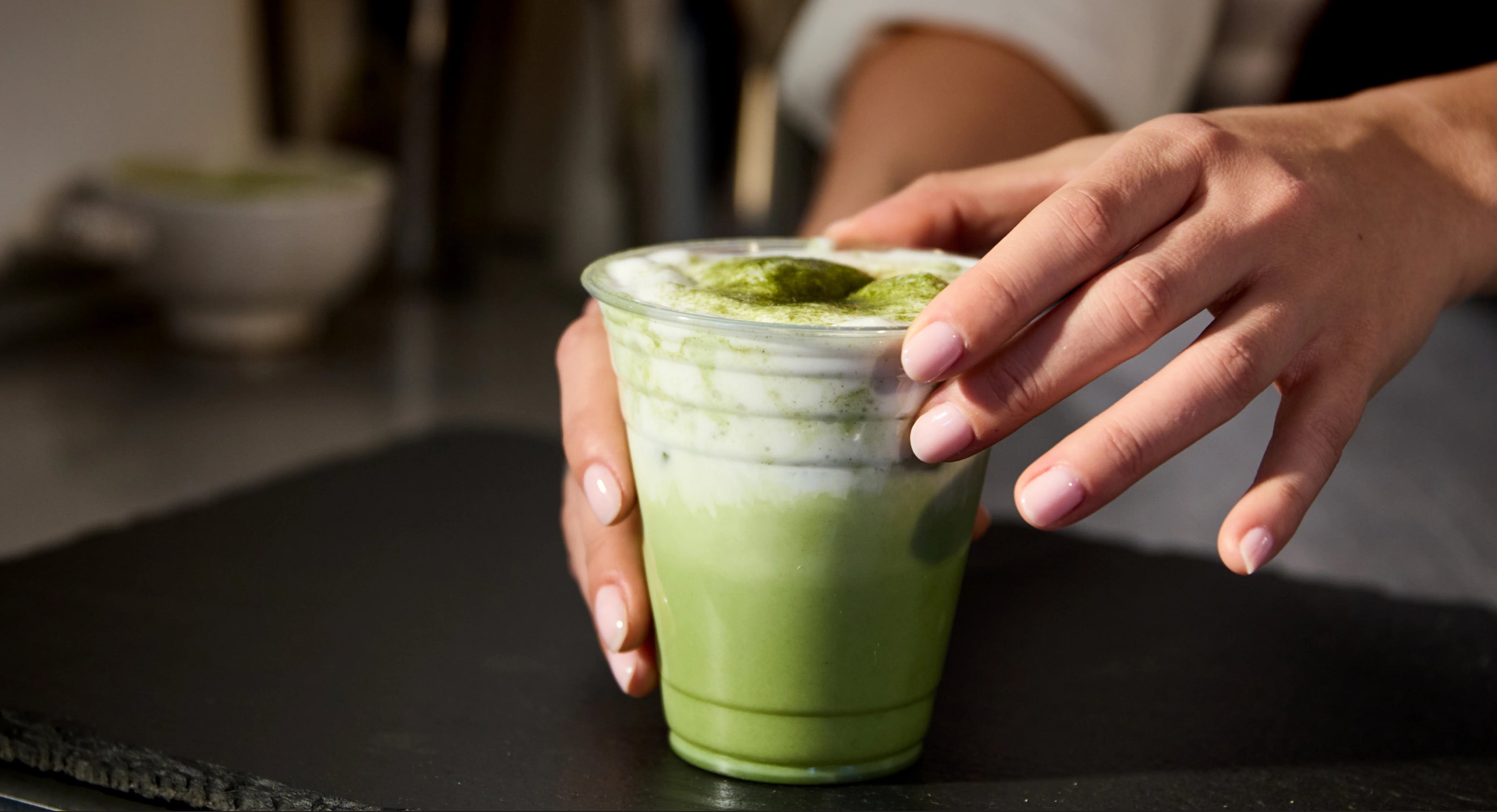 Person holding a glass of green matcha latte on a dark surface