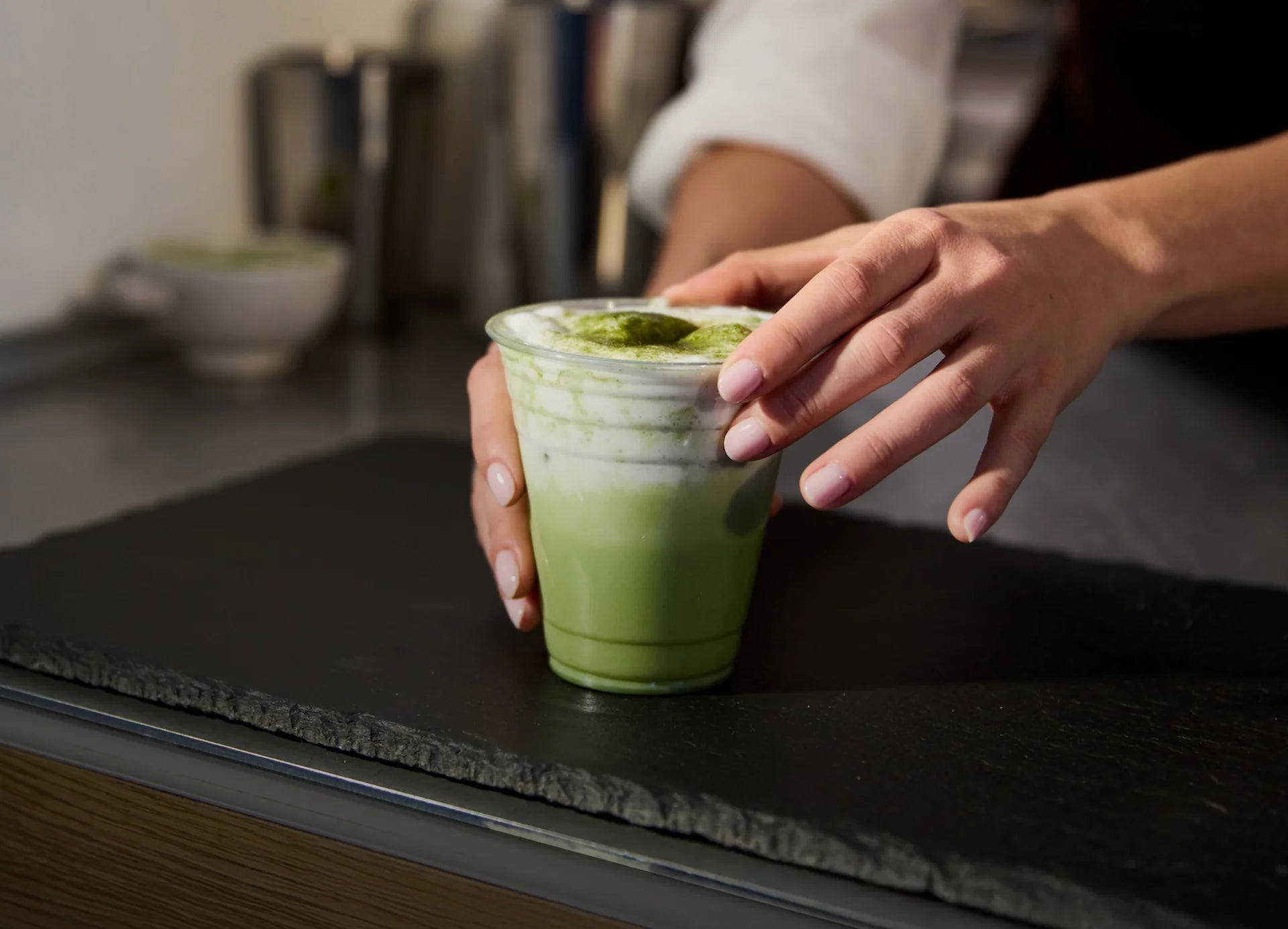 Person holding a green drink in a clear cup on a dark surface