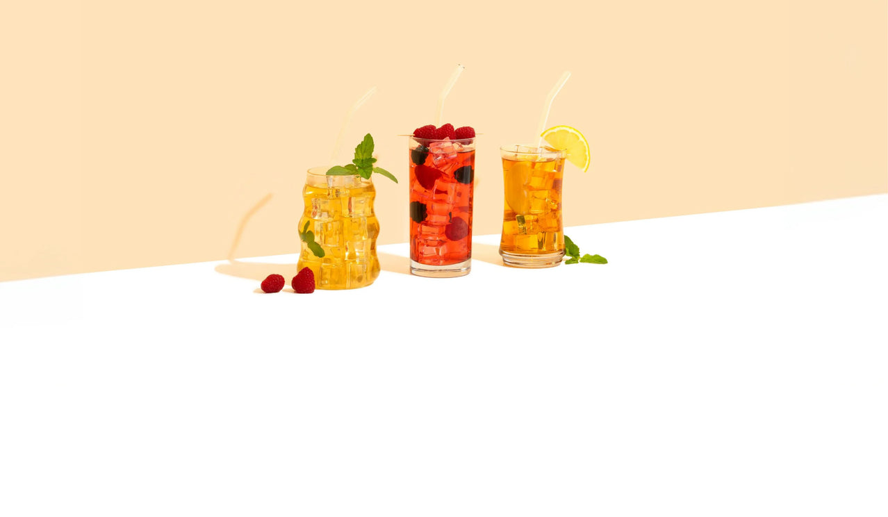 Three glasses of iced tea with berries and lemon slices on a white surface with a beige background
