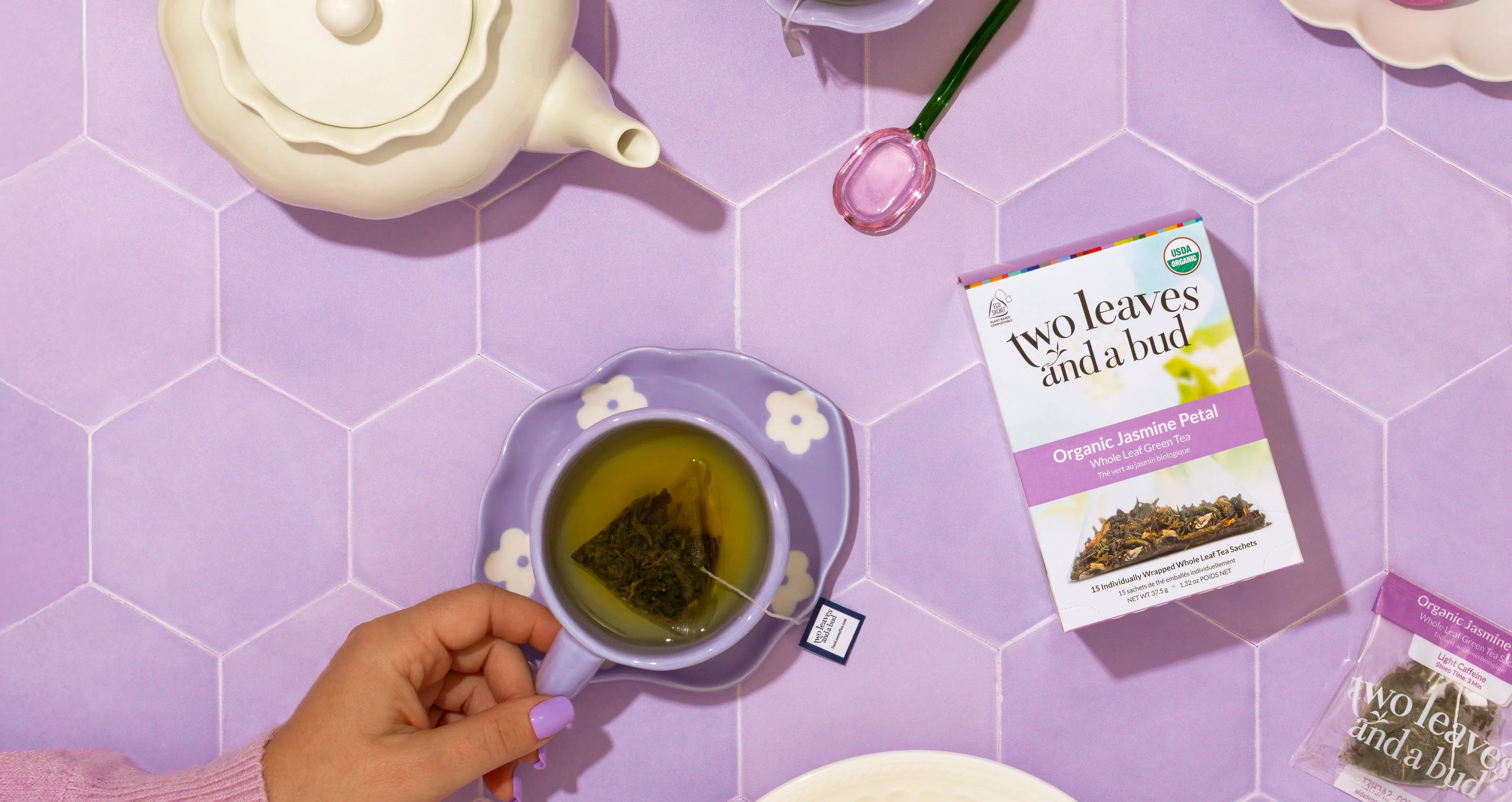 Tea cup with tea leaves, 'Two Leaves and a Bud' package on a purple tiled background