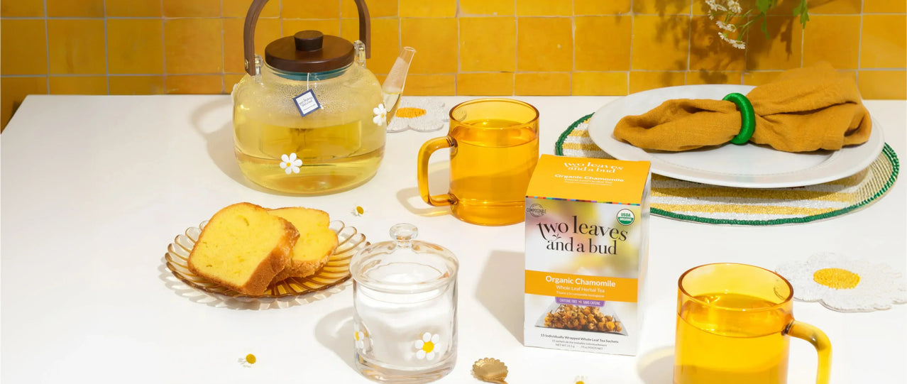 Tea-making setup with teapot, cups, and a package of tea leaves on a yellow-tiled wall background.