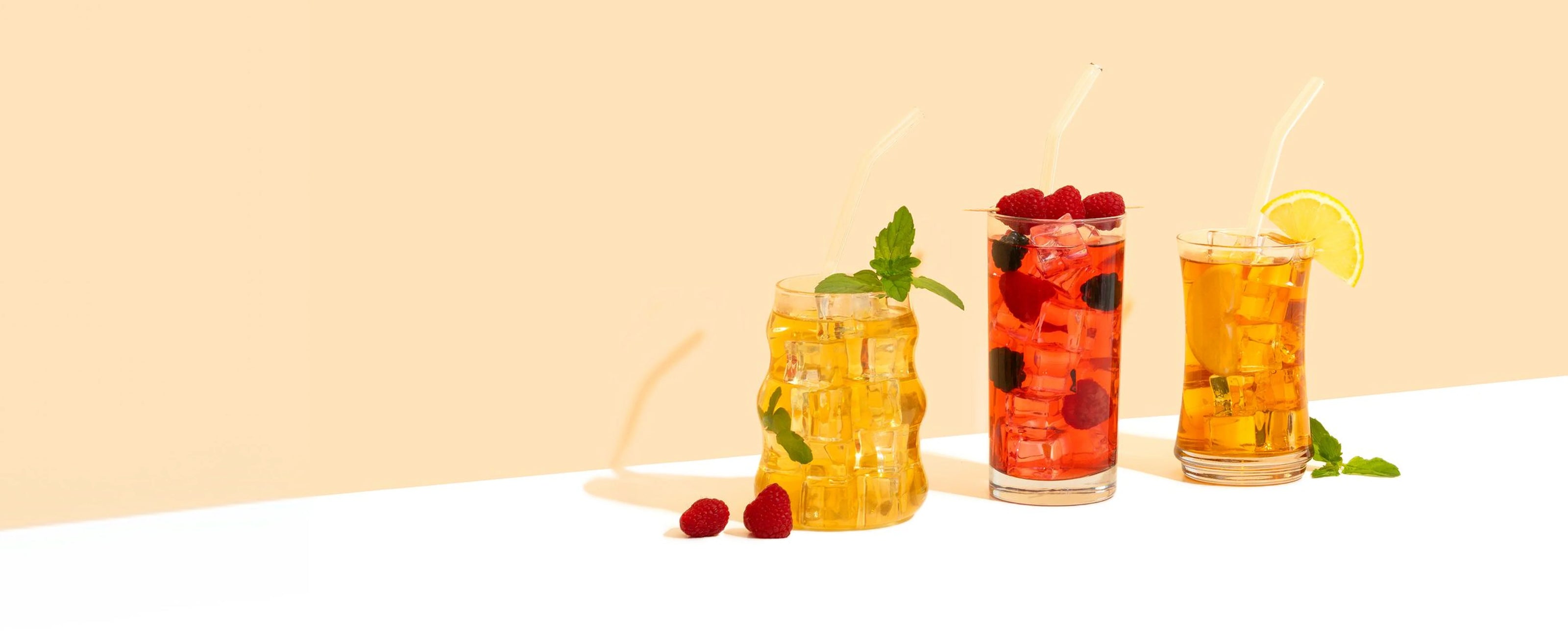 Three glasses of iced tea with berries and lemon slices on a light beige background