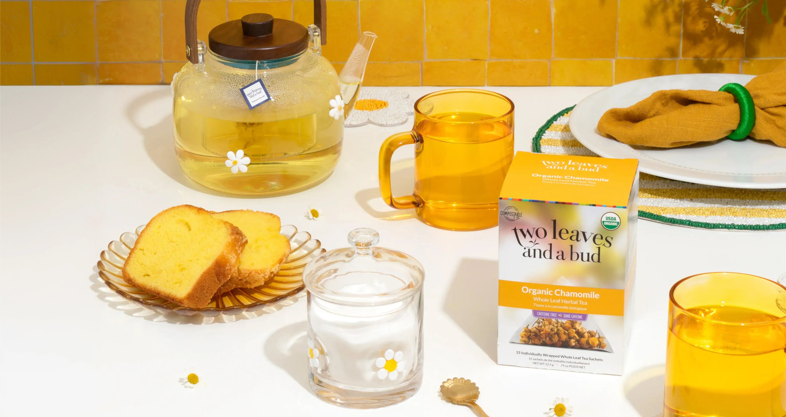 Tea-making setup with a teapot, cups, and a box of 'Two Leaves and a Bud' tea on a table.
